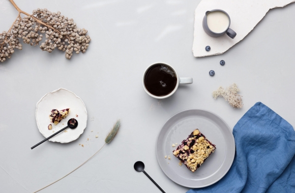 Mustikkapiirakkaa ja kahvia tarjolla pöydällä, jossa sinisiä somisteita